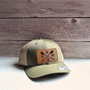 May include: A green and tan trucker hat with a brown leather patch featuring a compass design and the letters "N", "W", "P", and "S".