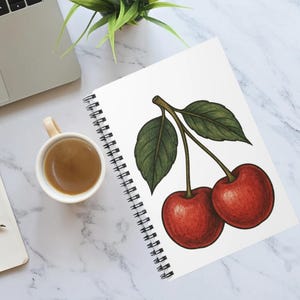 May include: A white spiral bound notebook with a drawing of two red cherries with green leaves on the cover.