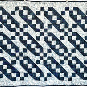 May include: A handmade quilt with a repeating pattern of dark blue and white squares arranged in diagonal lines. The quilt has a light blue paisley border and is hanging from a clothesline.