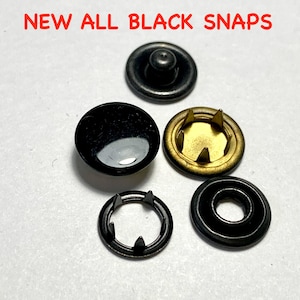 May include: A set of four black snap fasteners. The set includes two black snaps with a gold-colored center, one black snap with a black center, and one black snap with a black ring.