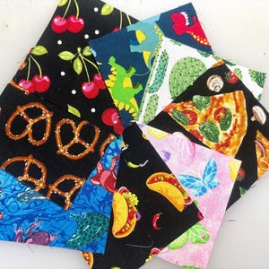May include: A collection of square fabric swatches featuring diverse patterns including red cherries on black, green dinosaurs, cacti, pizza slices, soft pretzels, blue frogs on water, tacos, and blue butterflies on a light pink background.