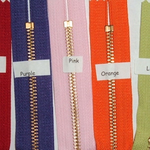May include: A close-up of seven different colored zippers with gold metal teeth. The zippers are labeled "Yellow", "Red", "Purple", "Pink", "Orange", "Light Green", and "Lavender".
