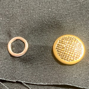May include: Two metal buttons, one round and one with a textured design. The round button is silver and the textured button is gold.