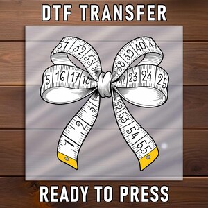 May include: A DTF transfer design featuring a bow made from a measuring tape. The tape is white with black markings and yellow accents. The text "DTF TRANSFER" and "READY TO PRESS" are at the top and bottom.