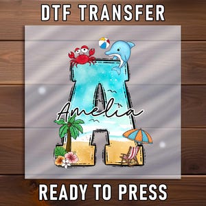 May include: DTF transfer featuring a beach-themed design with the name "Amelia" inside a letter "A". The design includes a crab, dolphin, beach ball, palm tree, beach chair, and umbrella. The words "DTF TRANSFER" and "READY TO PRESS" are at the top and bottom.