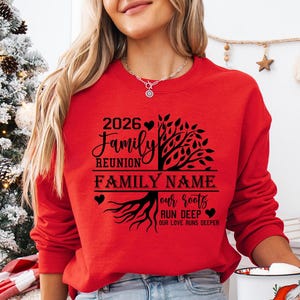 A woman wearing a red sweater with a tree design and text on it, standing in front of a Christmas tree.