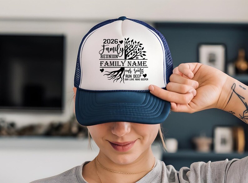 A person is holding up a blue and white baseball cap with a family name and a tree design on it.
