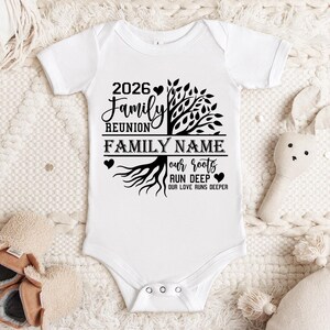 A white onesie with a tree design and text printed on it, placed on a white blanket.
