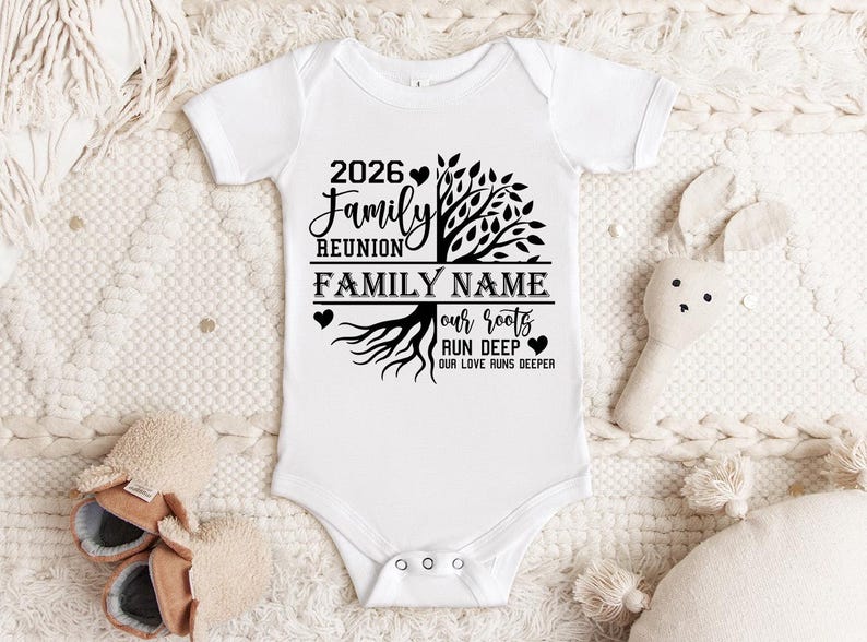 A white onesie with a tree design and text printed on it, placed on a white blanket.