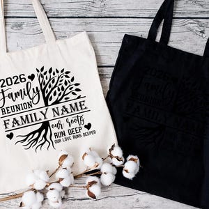 Two tote bags with a family tree design and text printed on them, placed on a wooden surface with cotton bolls in the foreground.
