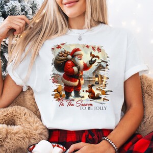 a woman wearing a santa clause t - shirt while holding a teddy bear