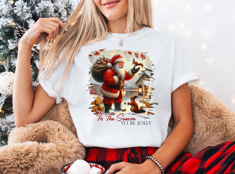 a woman wearing a santa clause t - shirt while holding a teddy bear