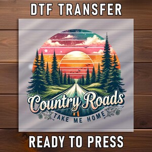 May include: DTF transfer design featuring a sunset over a road leading through a forest. The design includes the text "Country Roads Take Me Home" in a stylized font. The words "DTF TRANSFER" and "READY TO PRESS" are also included.