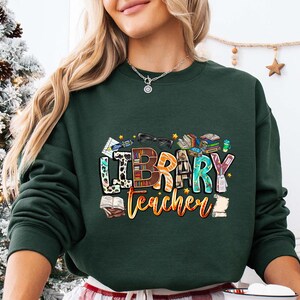 a woman wearing a merry teacher sweatshirt in front of a christmas tree