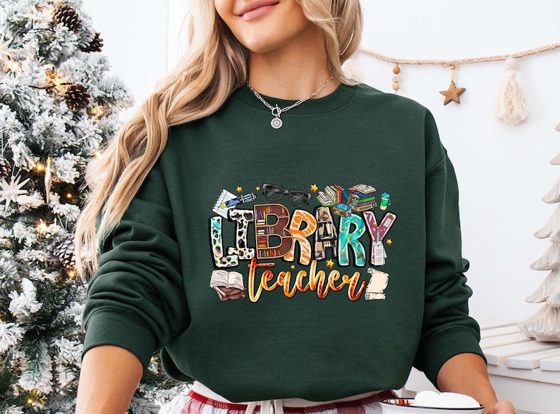 a woman wearing a merry teacher sweatshirt in front of a christmas tree