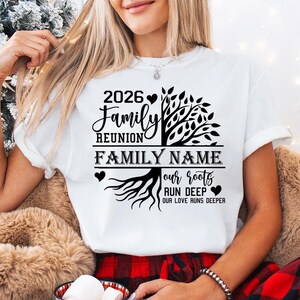 A woman wearing a white t-shirt with a graphic design on it, sitting in front of a Christmas tree.