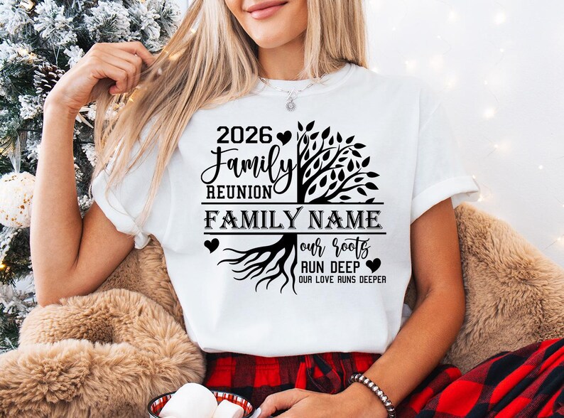 A woman wearing a white t-shirt with a graphic design on it, sitting in front of a Christmas tree.