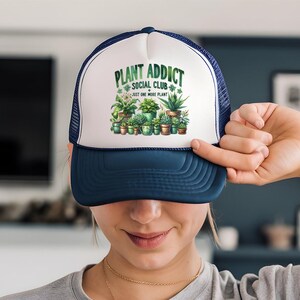 a woman holding up a trucker hat with plants on it