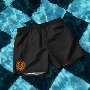 May include: Black swim trunks with an orange Bitcoin logo inside a laurel wreath on the left leg. The shorts have an elastic waistband and are shown against a background of blue and white checkered water.