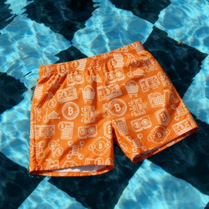 May include: Orange swim trunks with a white Bitcoin-themed pattern. The design includes Bitcoin symbols, shopping carts, and computer screens. The shorts are shown in a pool with a checkered pattern.