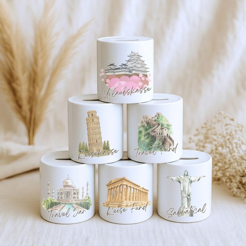 May include: White ceramic money banks with travel-themed illustrations. Each bank features a different landmark: a Japanese castle, the Leaning Tower of Pisa, the Great Wall of China, the Taj Mahal, a Greek temple, and Christ the Redeemer. Text includes "Travel Jar" and "Sabbatical".