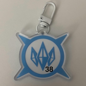 May include: A clear, blue and white keychain with a silver clasp. The keychain has a circular design with a blue outline and a white center. Inside the circle are three blue diamond shapes. The number "38" is printed in black.