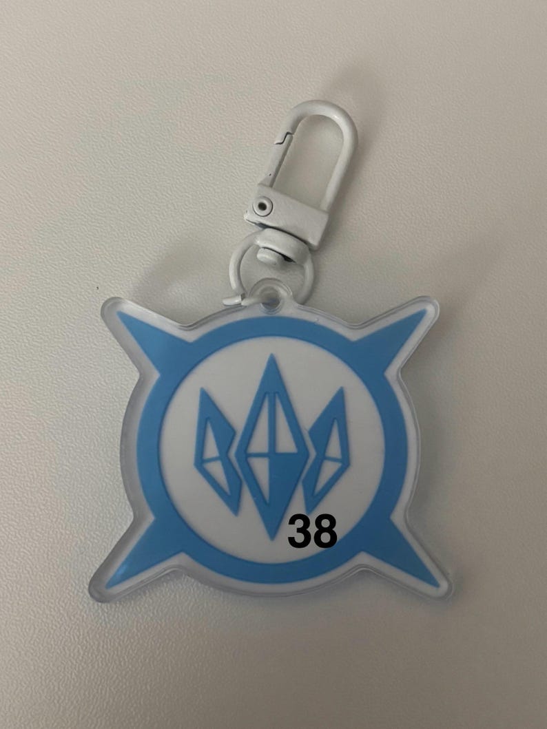 May include: A clear, blue and white keychain with a silver clasp. The keychain has a circular design with a blue outline and a white center. Inside the circle are three blue diamond shapes. The number "38" is printed in black.