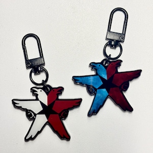 Puede incluir: Dos llaveros en forma de estrella con un diseño de pájaro. Un llavero presenta un diseño de pájaro blanco y rojo, mientras que el otro tiene un diseño de pájaro azul y rojo. Ambos llaveros tienen un cierre negro.