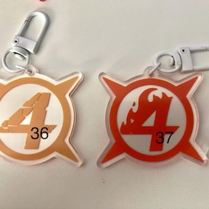 May include: Two keychains with white metal clasps. One keychain is orange with a white circle and the number 4, with the number 36 below. The other is red with a white circle and the number 4, with the number 37 below.