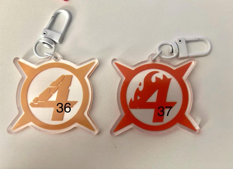 May include: Two keychains with white metal clasps. One keychain is orange with a white circle and the number 4, with the number 36 below. The other is red with a white circle and the number 4, with the number 37 below.