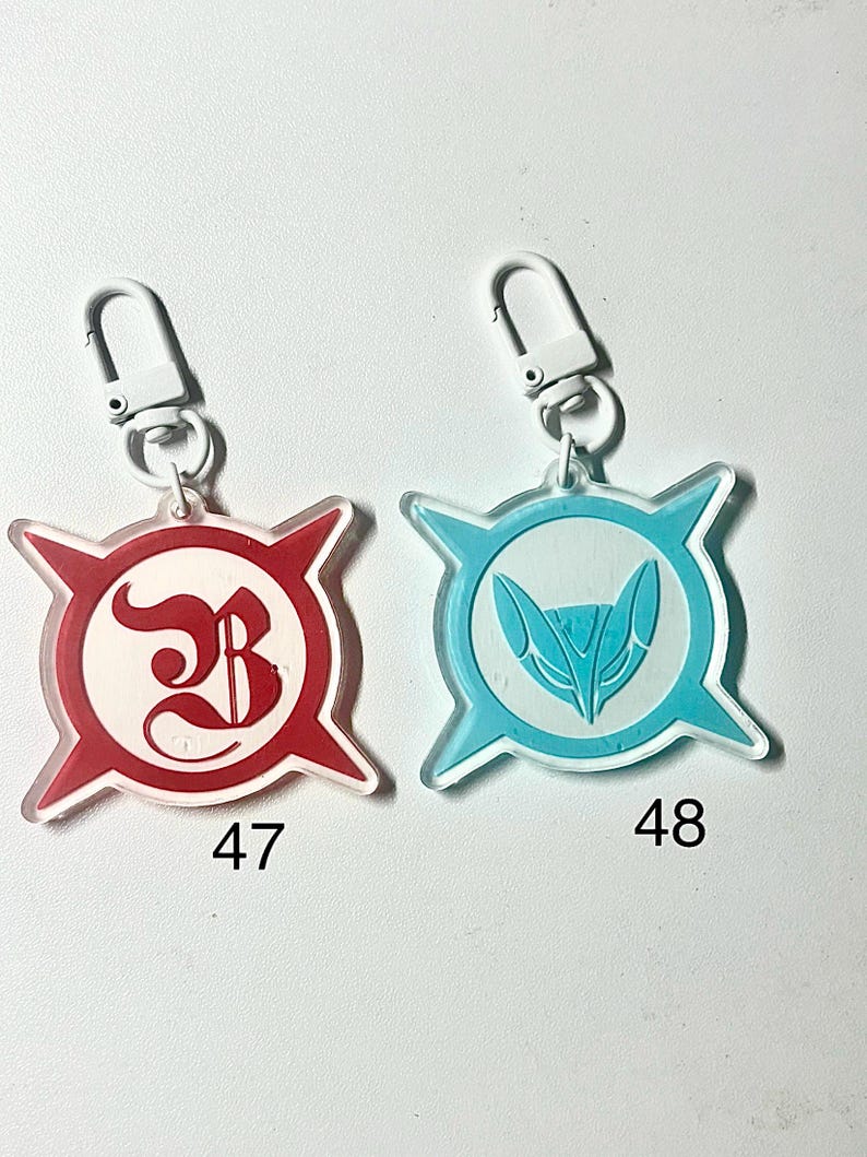 May include: Two keychains with clear plastic bodies and silver-colored clasps. One keychain has a red and white design with the number 47. The other has a blue and white design with the number 48. Both keychains have a starburst shape.