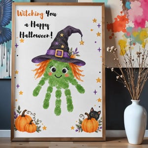 May include: A framed wall art print featuring a green handprint character wearing a purple witch hat with orange hair. The text reads Witching You a Happy Halloween! The design includes orange pumpkins, a black cat, and yellow stars on white.