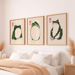 May include: Three framed prints with green frog illustrations. The first print shows a frog sitting with its legs crossed. The second print shows a frog sitting in a circle. The third print shows a frog holding a bowl.