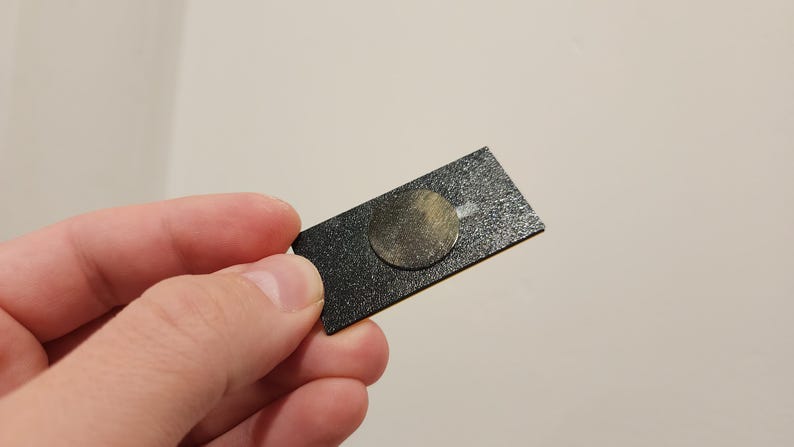 May include: A black rectangular adhesive pad with a round, gold-colored adhesive disc in the center.