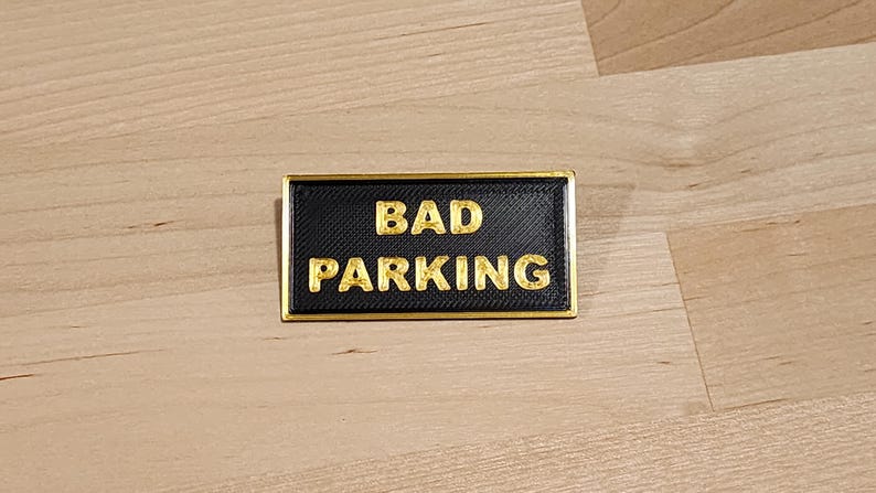 May include: A black rectangular sign with a gold border and the text "BAD PARKING" in gold letters.