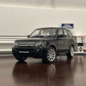 Puede incluir: Modelo de coche Range Rover Sport negro con detalles plateados. El coche tiene una parrilla negra con las palabras "RANGE ROVER SPORT" impresas en ella.