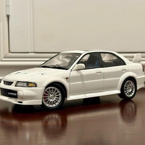 May include: A white model car with the word "Lancer" on the front. The car has a spoiler, red brake calipers, and silver rims. The car is a sedan.