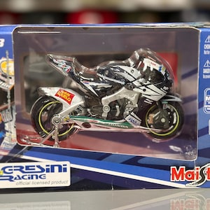 May include: A 1:18 scale die-cast metal model motorcycle in a display box. The motorcycle is black, white, and silver with sponsor logos. The box features the Gresini Racing logo and the Maisto brand.