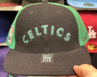 Può includere: Un cappellino da baseball nero e verde dei Boston Celtics. La parola "CELTICS" è ricamata in verde sul davanti. Il cappellino ha una visiera verde e il logo Nike Swoosh Flex è visibile.