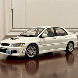 Może przedstawiać: Biały model samochodu Mitsubishi Lancer Evolution z czarną atrapą chłodnicy i czarnymi lusterkami bocznymi. Samochód ma czarne tablice rejestracyjne z tekstem "2NZ-8175".