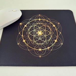May include: A black mouse pad with a gold geometric design featuring overlapping circles, squares, and lines. The design has a glowing effect.