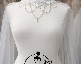 May include: A white bridal mannequin displays a delicate lace collar with pearl accents and a dangling teardrop pendant. A sheer veil drapes from the shoulders. The mannequin has a logo that says "Hana Novias Bridal".
