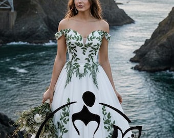 May include: A white wedding dress with green leaf accents and a flowing skirt. The off-the-shoulder bodice features a deep V-neckline. The dress is adorned with a floral design and the text "Hana Novias Bridal".