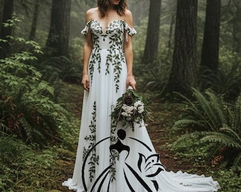 May include: A white wedding dress with a flowing train and off-the-shoulder sleeves. The dress is adorned with green leaf-like embroidery. The bride is holding a bouquet of flowers and greenery. The background is a forest setting.