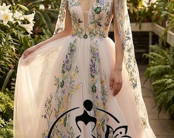 May include: A blush-colored wedding gown with floral embroidery in yellow, purple, and green. The dress features a plunging neckline and sheer cape sleeves. The text "Hana Novias BRIDAL" is displayed at the bottom of the dress.