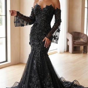 Op de afbeelding: Een zwarte off-the-shoulder jurk met lange, doorschijnende mouwen. De jurk heeft bloemversieringen en een zeemeerminsilhouet met een vloeiende sleep. De jurk is geschikt voor formele evenementen.