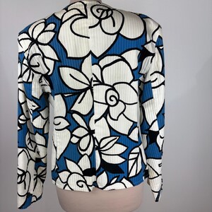 Puede incluir: Una chaqueta de traje de manga larga con estampado floral blanco y azul. La chaqueta tiene una textura acanalada y una silueta ligeramente ajustada.