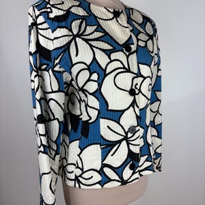 Puede incluir: Una chaqueta con estampado floral azul y blanco con cierre de botones. La chaqueta tiene una textura acanalada y mangas largas.