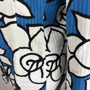 Puede incluir: Una chaqueta con estampado blanco y azul con un dise&ntilde;o floral negro. La chaqueta tiene una textura acanalada y un cierre de bot&oacute;n.