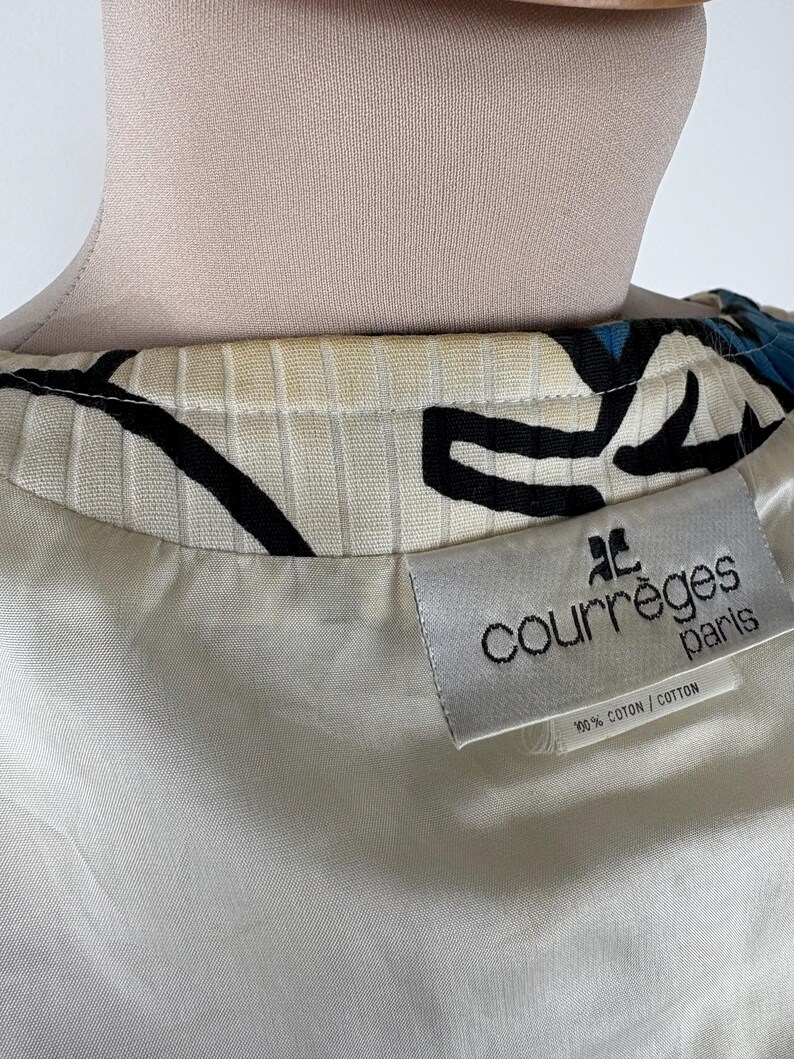 Puede incluir: Una tela de patr&oacute;n blanco y negro con un acento azul. La tela tiene una etiqueta blanca con el texto "Courr&egrave;ges Paris" y "100% Algod&oacute;n/Algod&oacute;n".